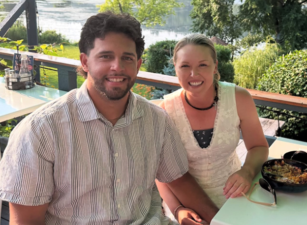Brooke Henderson and Ricky Castro sitting side by side on an outdoor patio. With a lake in the background.
