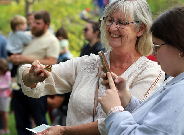 Woman smiles as she gently holds a butterfly during a community memorial event, surrounded by others gathering to release butterflies.