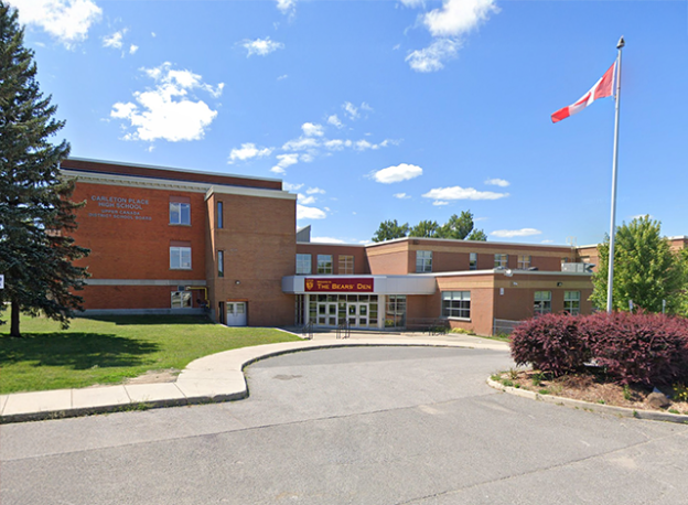A large, red-brick high school building with a circular driveway in front. A Canadian flag flies from a pole on the right, and the sign above the entrance reads "Carleton Place High School - Home of The Bear's Den." This building is an example of a strategic property being discussed by the town council.