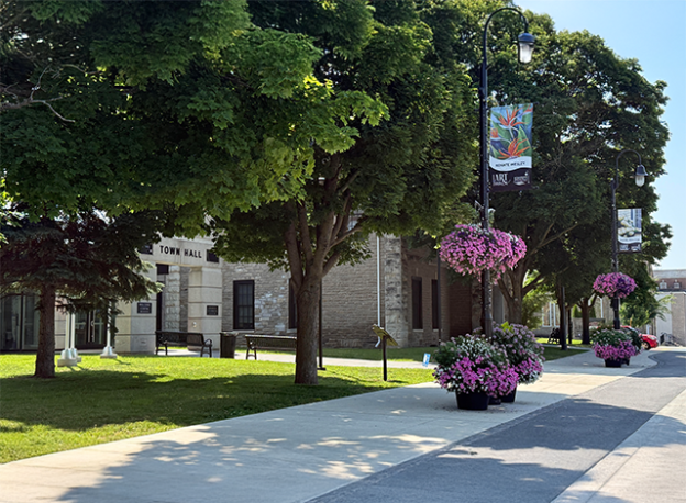Green trees and purple flower planters sitting around and hanging on light posts just outside of Smiths Falls town hall where council keeps CIP fall intake deadline at Sept. 1 with $13,600 in available funding.